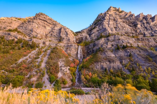 A scenic view of a waterfall cascading down rocky mountains, surrounded by lush greenery and colorful autumn foliage.
