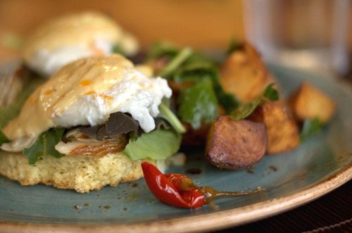 A plate of poached eggs on greens with roasted potatoes and a red chili pepper garnish.