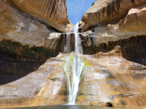 A stunning waterfall cascades down a rocky cliff into a serene pool below, surrounded by natural rock formations.