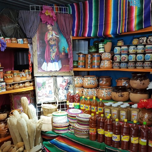 Colorful market stall displaying traditional pottery, woven baskets, and decorative items with vibrant textiles in the background.
