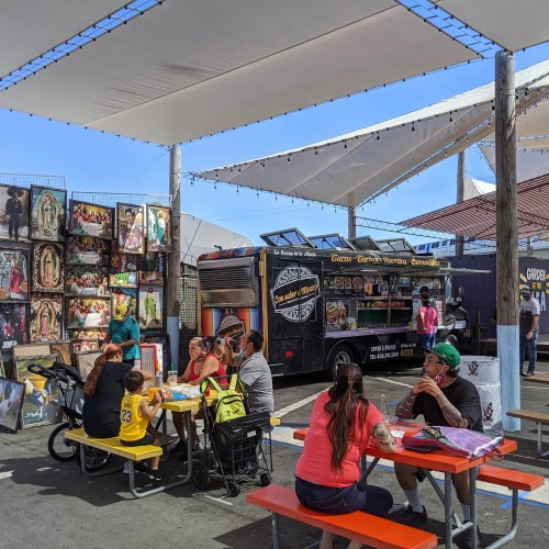 A vibrant food truck area with families dining at colorful tables under a canopy, surrounded by art displays.