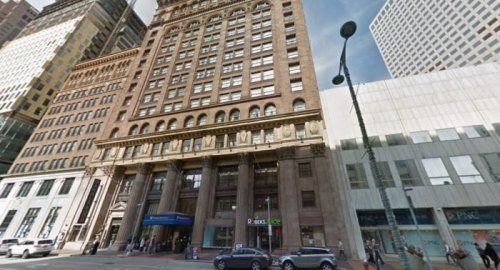 Historic building with ornate architecture, tall columns, and modern structures nearby in an urban setting.