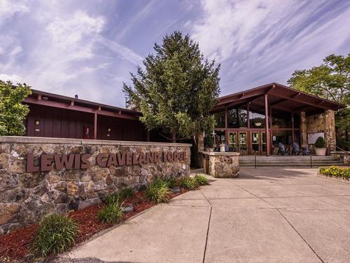 Exterior view of Lewis Caverns Lodge, featuring stone walls, large windows, and surrounding greenery under a cloudy sky.