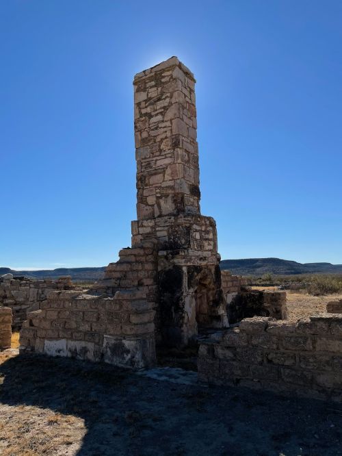 A tall stone chimney stands amidst the ruins of a structure against a clear blue sky.