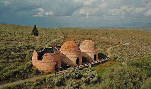 Three dome-shaped, weathered structures sit on a grassy hillside under a cloudy sky, surrounded by sparse vegetation.