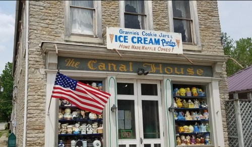 A stone building with an ice cream parlor sign, featuring a display of cookie jars and an American flag.