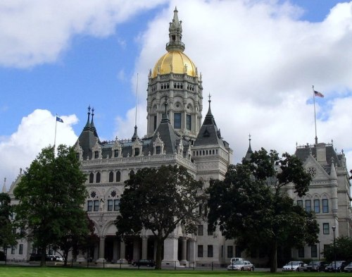 The Connecticut State Capitol building with a golden dome, surrounded by trees and a cloudy sky.