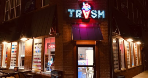 A brightly lit ice cream shop named "TRASH" with a neon sign, featuring large windows and an inviting entrance.