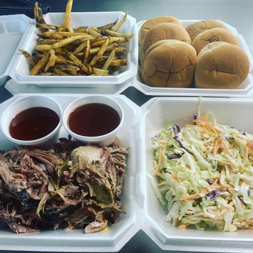 A takeout meal featuring pulled pork, coleslaw, fries, and slider buns in divided containers.