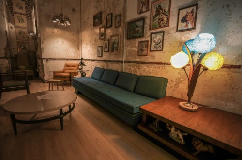 A cozy, vintage-inspired living room with a blue sofa, wooden coffee table, and colorful lamp against a textured wall.