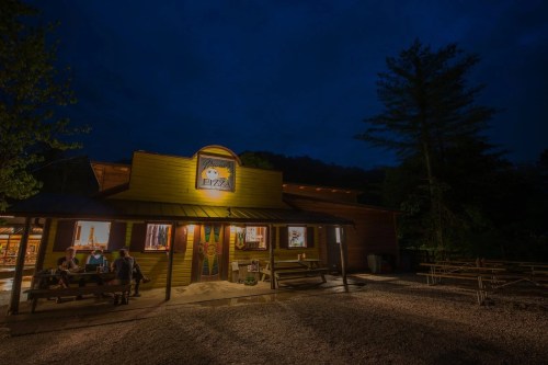 A cozy pizza restaurant at night, with outdoor seating and warm lights glowing from the windows.