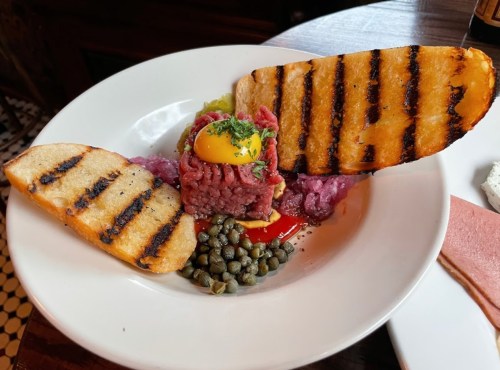 A plate with grilled bread, raw beef tartare topped with an egg yolk, capers, and purple onions.
