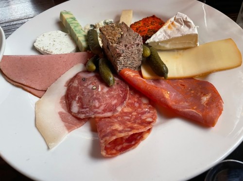 A platter of assorted meats, cheeses, pickles, and spreads arranged on a white plate.
