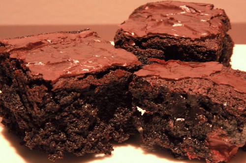 Three rich, fudgy chocolate brownies stacked on a white plate, showcasing a glossy, cracked top.