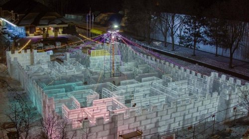 Aerial view of a large ice maze illuminated with colorful lights, surrounded by snow and trees.