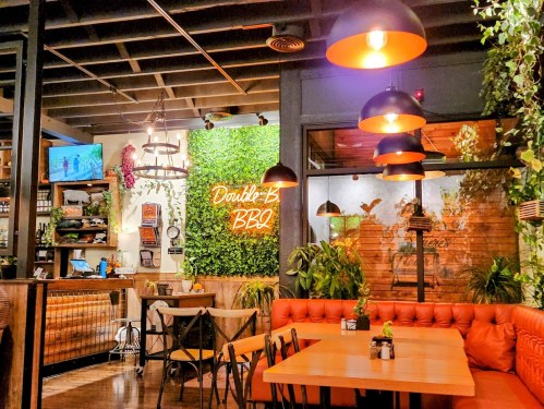 Cozy restaurant interior with green wall decor, neon sign reading "Double-B BBQ," and warm lighting.
