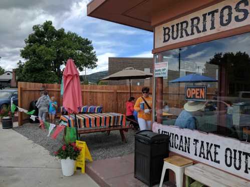 A colorful outdoor seating area at a burrito takeout, with people dining and enjoying the sunny day.