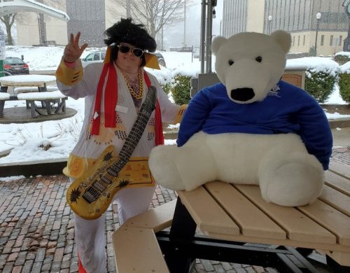 A person in an Elvis costume poses with a large polar bear plush toy in a snowy outdoor setting.