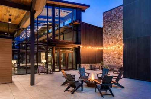 Modern outdoor patio with a fire pit, surrounded by chairs and string lights, set against a contemporary building.