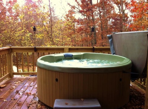 A hot tub on a wooden deck surrounded by autumn trees with colorful leaves.