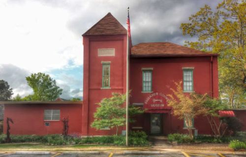 Red brick building with a tower, featuring a flagpole and trees, labeled as the Liberty County Museum.