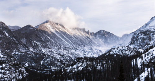 Snow-covered mountains under a cloudy sky, with mist rising from the valleys below.