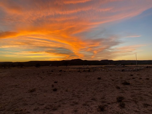 A vibrant sunset with swirling orange and pink clouds over a desert landscape and distant hills.