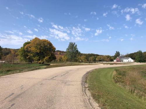 A winding road lined with trees and a house in a scenic landscape under a clear blue sky.