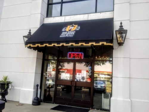 Entrance of East Camp Antiques with an "OPEN" sign and a black awning. Large windows and decorative lanterns are visible.