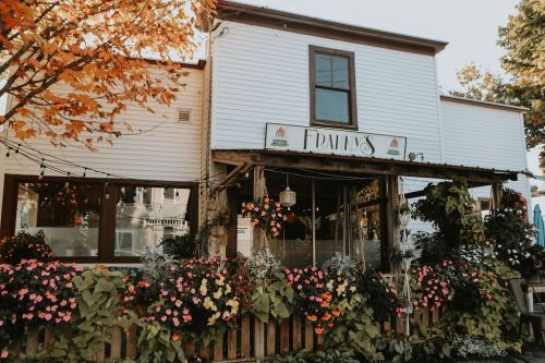 Charming restaurant exterior with colorful flowers, autumn leaves, and a welcoming sign.