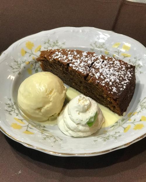 A slice of cake dusted with powdered sugar, served with two scoops of ice cream and a dollop of whipped cream.