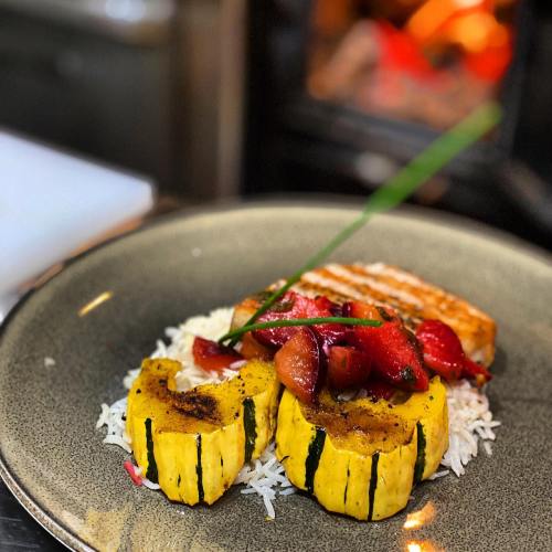 A plate of grilled squash and salmon on rice, topped with sautéed vegetables and garnished with a green onion.