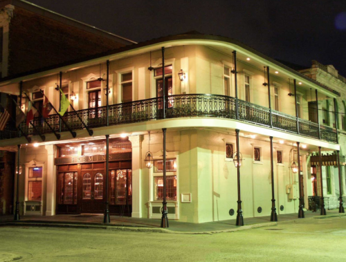 Historic building at night with a balcony, warm lighting, and flags, located in a vibrant urban setting.