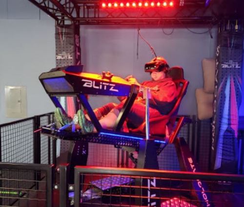 A person wearing a VR headset sits in a high-tech gaming chair with colorful lights in a gaming environment.