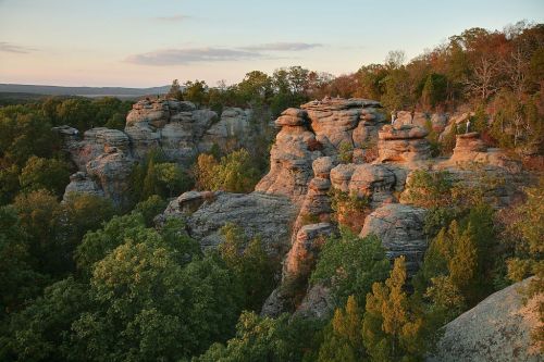 Rock formations surrounded by lush greenery under a sunset sky, showcasing natural beauty and rugged terrain.