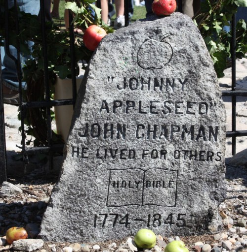 Gravestone of Johnny Appleseed, inscribed with his name, dates, and a quote about living for others, surrounded by apples.