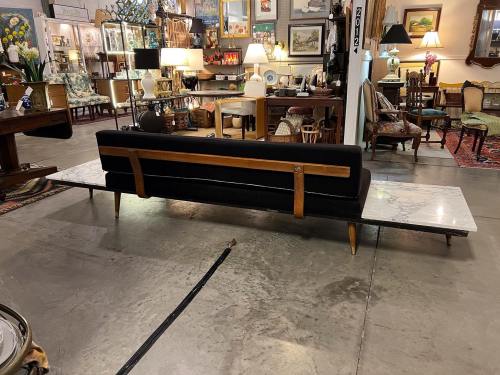 A modern black sofa with a wooden backrest, placed on a marble surface in a vintage furniture store.