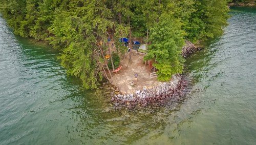 Aerial view of a small island with tents and trees, surrounded by calm water.