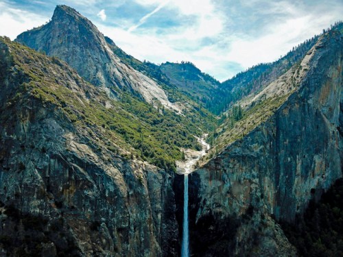 A stunning view of a waterfall cascading down rocky cliffs, surrounded by lush greenery and towering mountains.