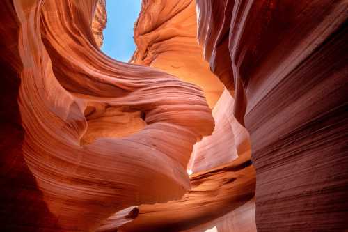 A stunning view of Antelope Canyon, showcasing swirling red rock formations and bright blue sky above.