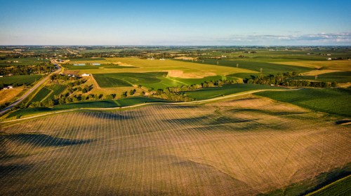 Aerial view of expansive farmland with fields, roads, and a clear blue sky in the background.