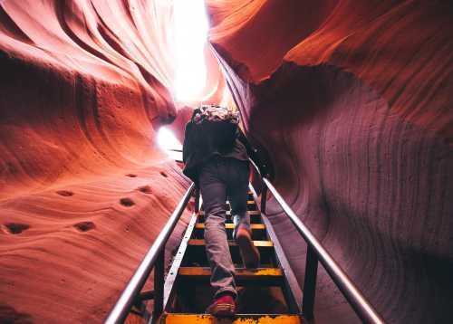 A person climbs stairs through a narrow, colorful canyon with smooth, curved rock walls.