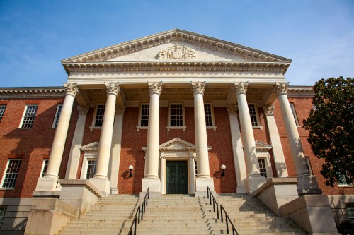 Historic building with a grand entrance, featuring tall columns and a pediment, set against a clear blue sky.