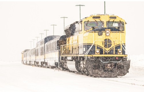 A yellow train is stopped in a snowy landscape, with heavy snowfall obscuring visibility.