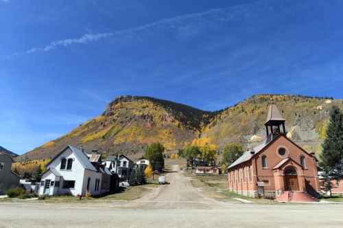 A scenic view of a small town with a church, surrounded by colorful autumn foliage and a mountain backdrop.