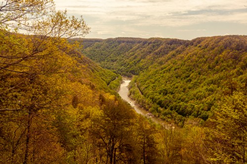 A scenic view of a winding river surrounded by lush green hills and trees under a cloudy sky.