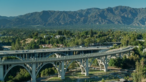 A scenic view of a bridge spanning a valley, surrounded by lush greenery and mountains in the background.