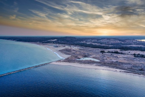 Aerial view of a serene coastline at sunset, with calm waters and sandy shores under a colorful sky.