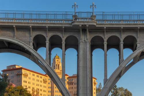 A view of a bridge with arches, featuring a building in the background illuminated by warm sunlight.