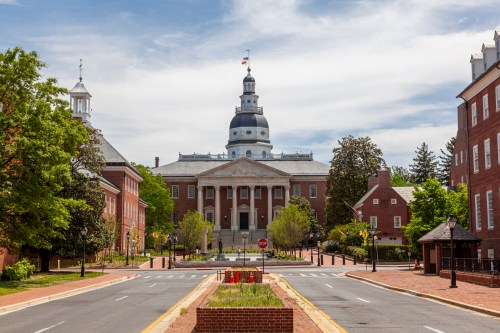 The Maryland State House, featuring a dome and surrounded by trees, with a clear blue sky above.